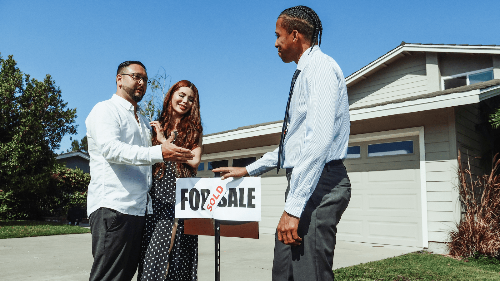 a young couple who bought a house and a realtor change the "for sale" sign to "sold"