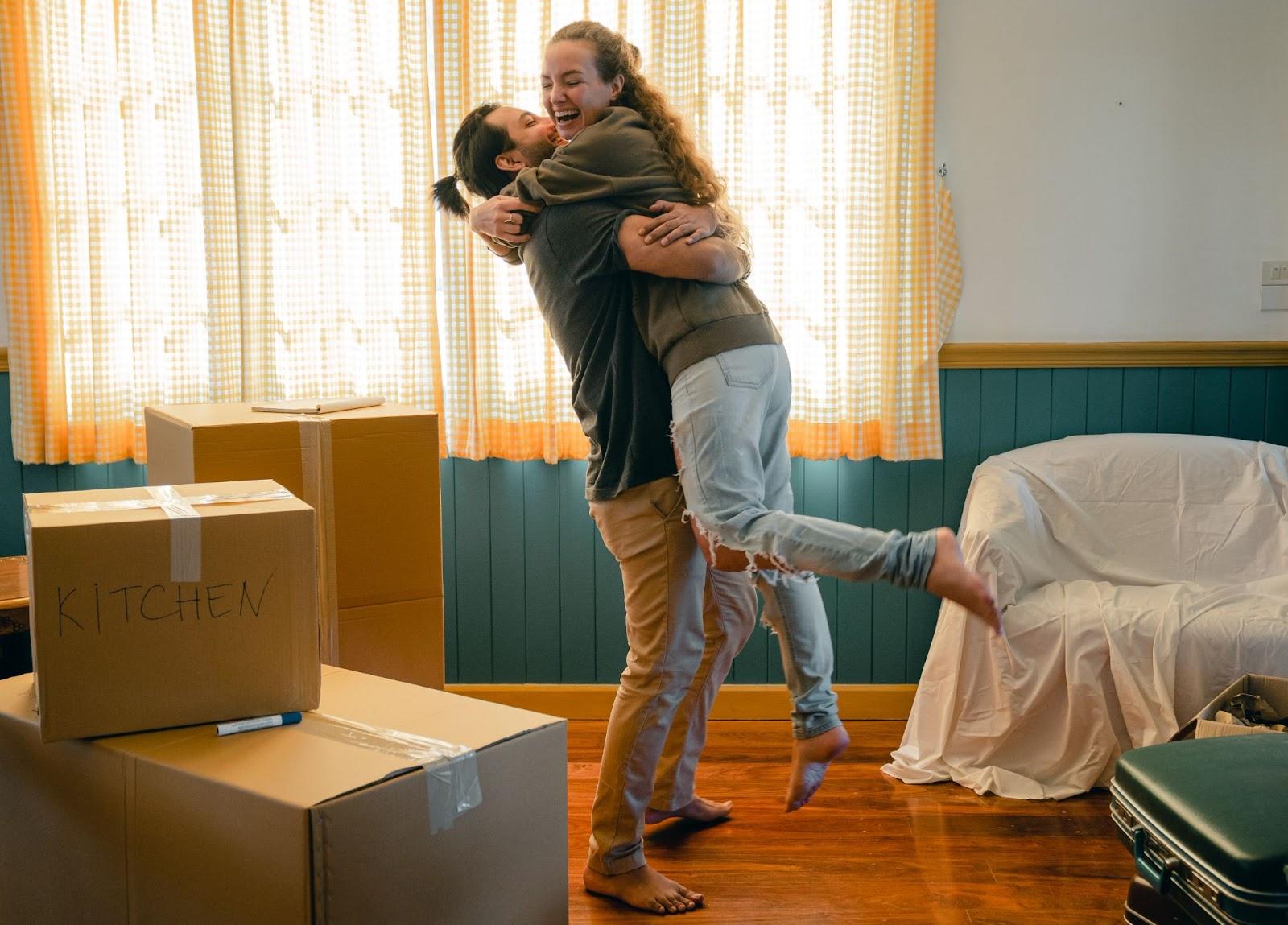 Guy holds a girl in his arms next to boxes of stuff for move-in another house