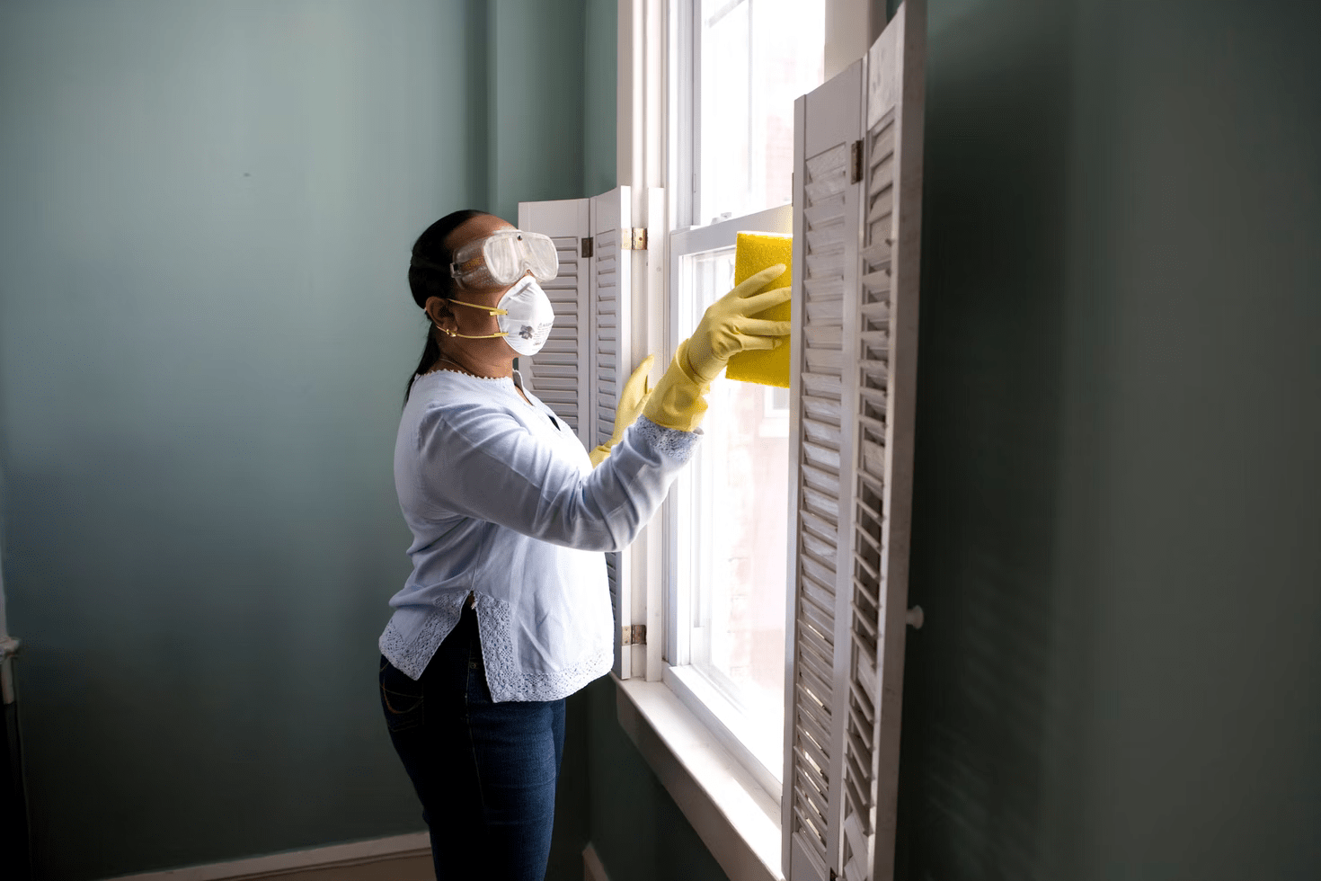 a woman in a mask and gloves washes the window