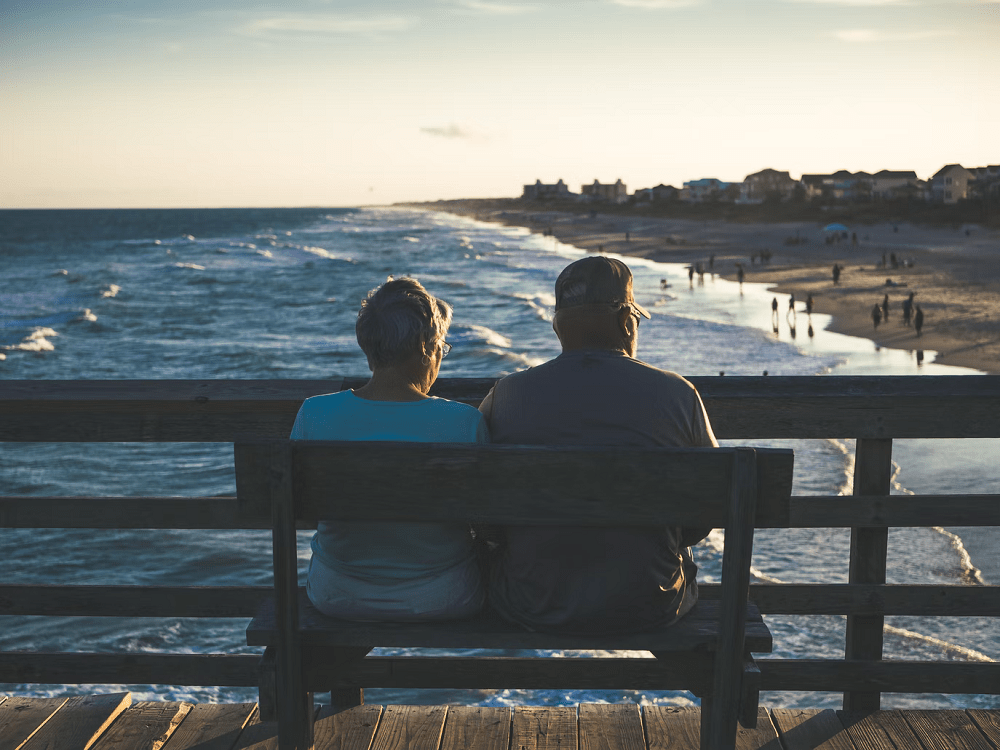 an adult couple sitting behind on a bench overlooking the sea