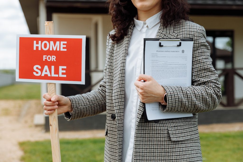 A realtor holding a home for sale sign in front of a listed property