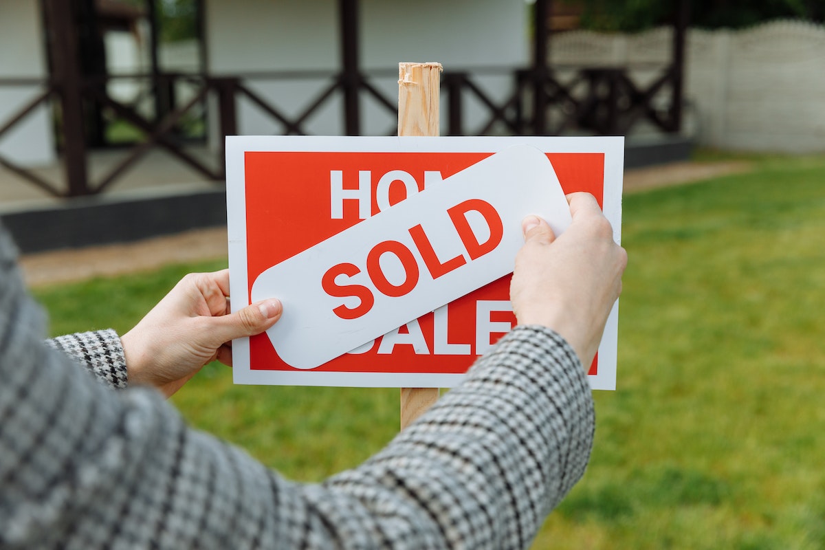 A man holding a SOLD card over a HOME FOR SALE sign.